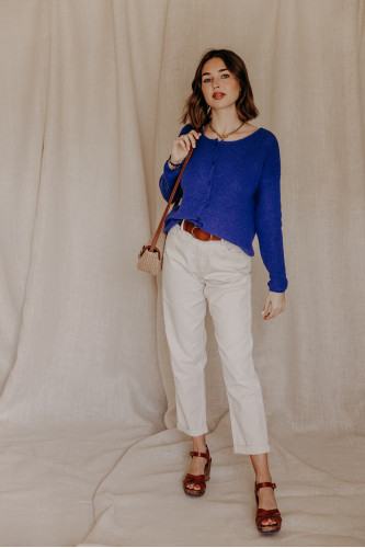 Femme avec un gilet bleu et un jean blanc.