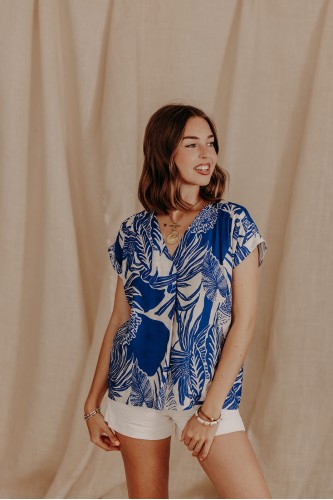 femme debout qui pose avec un top bleu à feuillages et un short blanc
