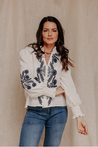 femme debout qui porte une chemise blanche brodée et un jean