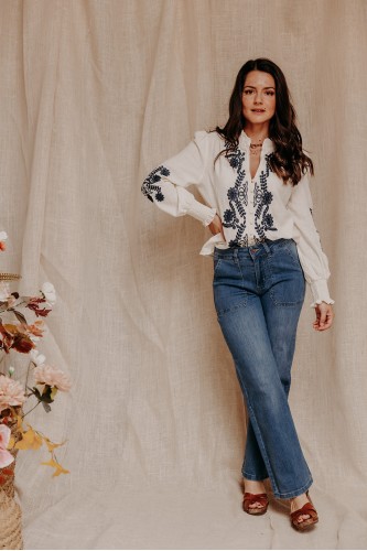 femme debout qui porte une chemise blanche à broderies et un jean