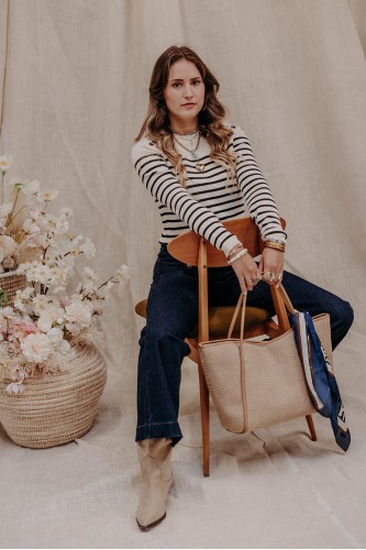 femme assise sur une chaise et qui porte un pull à rayures et un jean brut