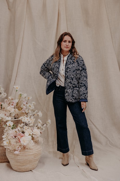 Femme debout qui porte une veste imprimée feuillages et un jean brut.