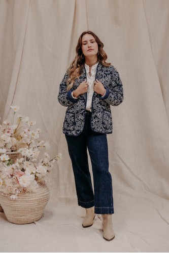 Femme debout qui porte une veste large à feuillages et un jean taille haute.