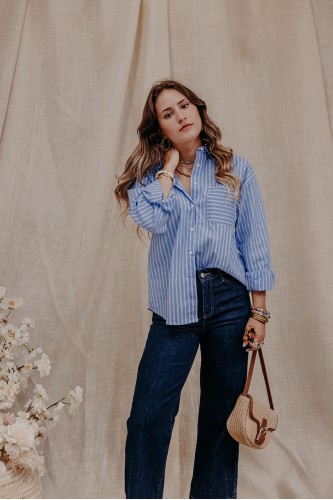 Femme debout qui porte une chemise bleu à rayures et un jean taille haute.