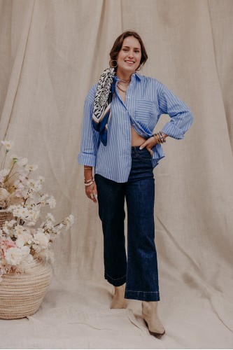 Femme debout qui porte une chemise rayée et un jean brut.