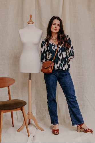 Femme debout qui porte une blouse imprimée et un jean.