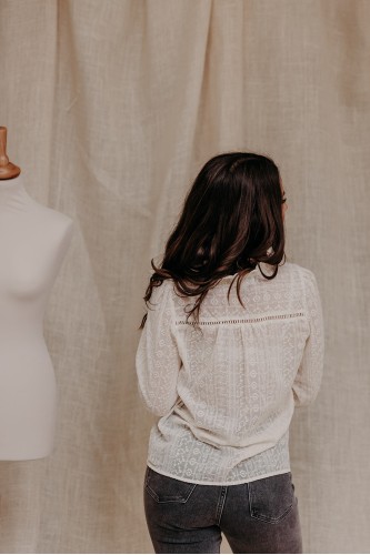 Dos d'une femme qui porte une chemise écru brodée et un pantalon gris.