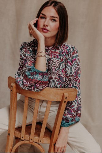 Femme assise avec une blouse imprimée.