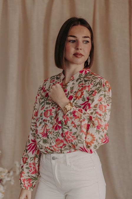 Blouse au print fleuri rentrer dans un pantalon blanc.